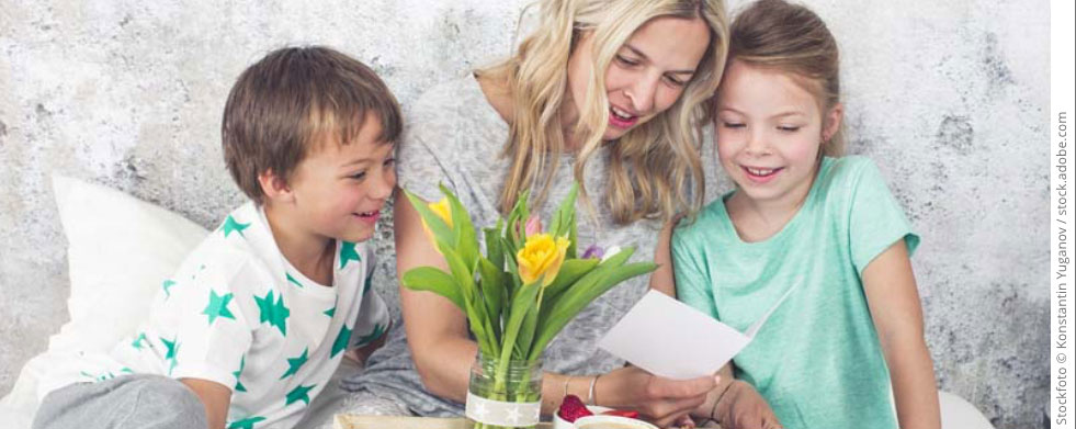 Frau mit zwei Kindern und Frühstückstablett und Blumen im Bett 